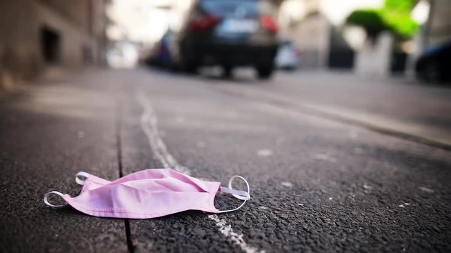 A used pink face protection mask lies abandoned on the pavement.
