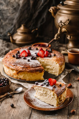 Homemade cheesecake or cottage cheese casserole with berries and icing sugar on rustic wooden table with samovar and teapot, complex composition. Sweet dessert, close up