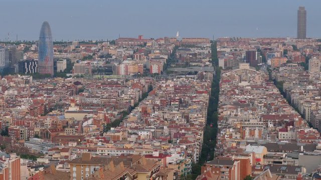 Straight lines of streets crossing dense build city, aerial view of Barcelona from top of hill. Typical cityscape of Eixample, Mediterranean sea waters seen on background