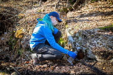 Ecologist taking water samples from a natural source in protective gloves and mask