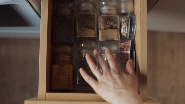 A young girl to choose spices in glass jars in the drawer of the kitchen table. Close-up