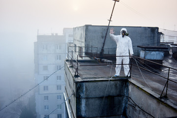 Researcher in protective suit and gas mask working on roof of high building, surrounded by power lines, showing stop sign, buildings on background