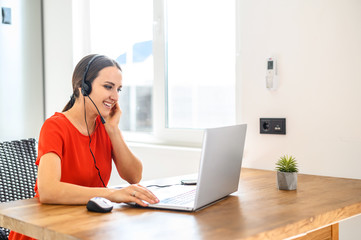 Young woman works from home using headset, laptop