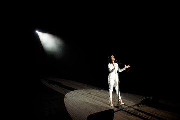 Singer woman on stage with black background in a beam of white light.