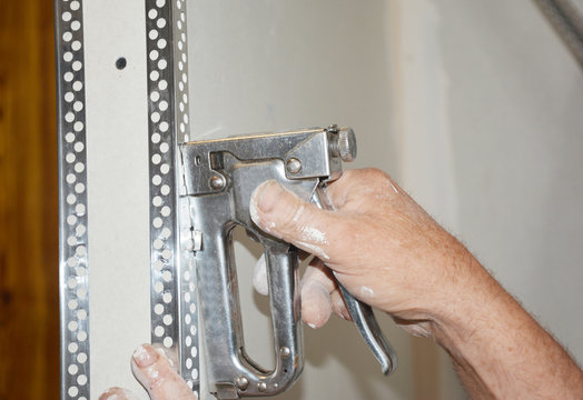 Renovating the house, a building contractor is fixing an angle bead, corner bead with a heavy duty stapler to the corner of the wall.
