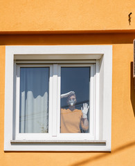Coronavirus. Woman in quarantine wearing protective mask and gloves looking through the window.  Stay home. Spring outdoor