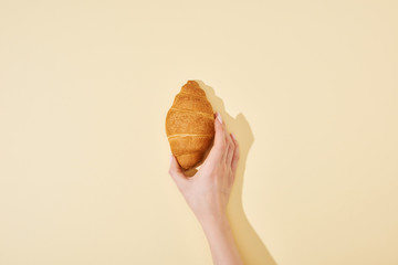 cropped view of woman holding fresh croissant on beige background
