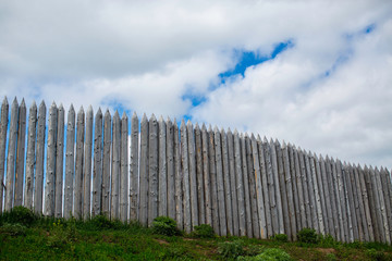 Fototapeta premium fortress wall of pointed logs against a cloudy sky