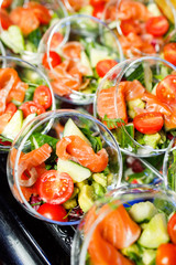 Top of buffet table with glass cups with salad of red fish, tomatoes, cucumber