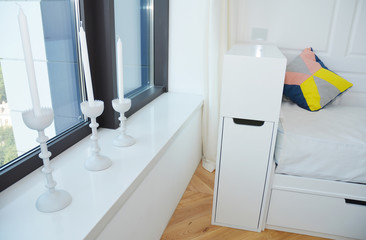 A stylish black and white interior a large window in black / gray, white window sill with candle holders, radiator cover, sofa and wooden laminated floor.