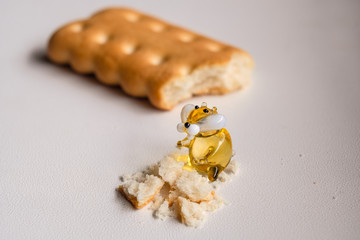 Macro photo of a small toy glass hamster standing next to cookie crumbs and a bitten cookie lies behind him