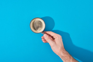 cropped view of man holding cup of fresh coffee on blue background