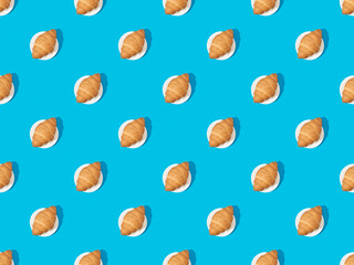 top view of fresh croissants on plates on blue, seamless background pattern