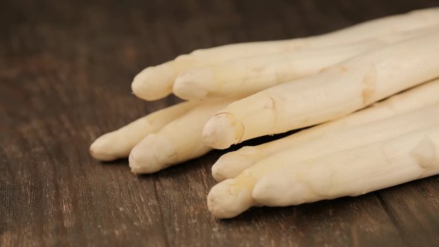 Woman puts bunch of raw white asparagus on wooden table. Healthy food.