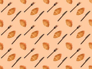 top view of cutlery and fresh croissants on orange, seamless background pattern