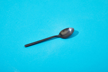 metal shiny black spoon on blue background