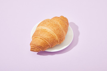 fresh tasty croissant on plate on violet background