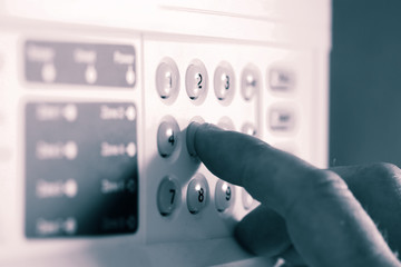 Man setting a security alarm by typing in a code on a keypad.  With colour toning
