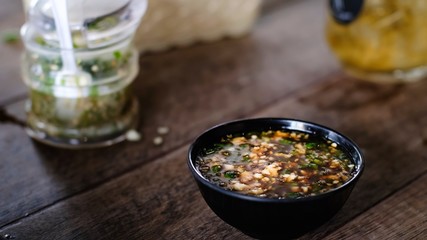 Close up shabu shabu spicy dip sauce topping with chilli in black bowl on wooden table in restaurant. Most popular food in thailand.