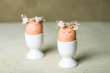 Natural easter eggs with funny painted face and sweet flower wreath in egg cup