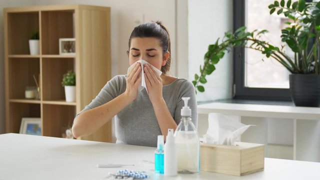 health care, virus and people concept - sick woman with medicines and sanitizers on table coughing and sneezing to paper tissue at home