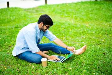 Naklejka na ściany i meble handsome young businessman relaxing and working on laptop computer on lawn at home. Work from home and social distancing concept