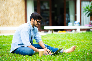 handsome young businessman relaxing and working on laptop computer on lawn at home. Work from home and social distancing concept