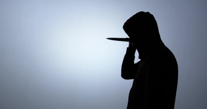 Silhouette of a man in a hood stabs with a knife from top to bottom