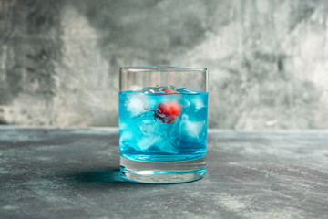 Blue old fashioned cocktail with cherry on the rustic background. Selective focus. Shallow depth of field.
