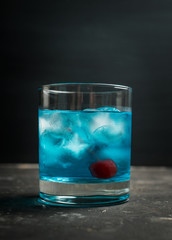 Blue old fashioned cocktail with cherry on the rustic background. Selective focus. Shallow depth of field.
