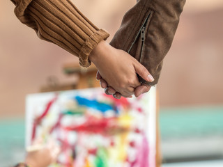 Selective focus on Couple holding hands while looking at artist paint the abstract painting. Valentine, love concept.