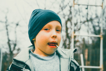 A European boy eats a delicious orange Lollipop. A contented and happy child loves sweets.