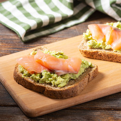 Bruschetta with avocado and salmon on a wooden Board on a brown wooden table. Toasted bread with avocado and red fish. The concept is useful and delicious Breakfast