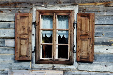 A window with open shutters on a rustic brown wooden wall. Reflection of the sky and trees in square panes. The Tokarnia open-air museum in Poland.