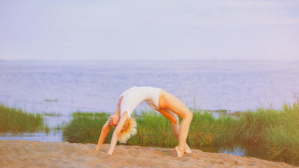 Young healthy woman practicing yoga pose on the beach at sunrise. Physical, spiritual, healthy, relaxing concept. Girl exercise and doing warm up posture stretching body at summer day on sea coast.