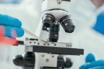 partial view of biochemist looking holding small stone with tweezers near microscope