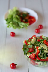 Salad on a white wooden background from tomatoes, cucumber, lettuce and red pepper. Healthy eating concept.