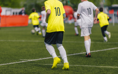 Back of junior football player playing game on the sports stadium. Footballers in soccer jerseys with numbers on the back