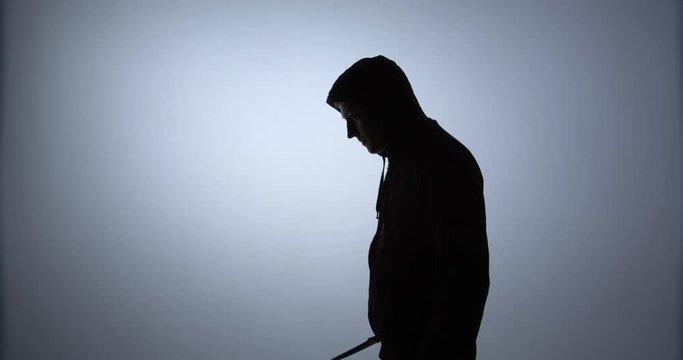 Silhouette of a man in a hood comes into the frame and threatens with a knife