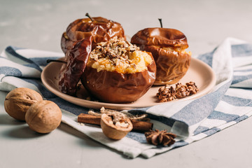 Baked apples with cottage cheese and dried fruits, the cook’s hands pour crushed walnuts, cinnamon on a wooden background close-up.