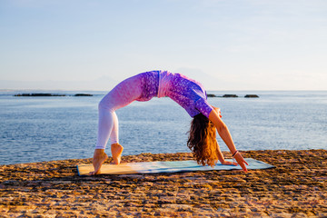 Young woman practicing Chakrasana or Urdhva Dhanurasana, Full Wheel Pose. Upward facing bow pose is a deep backbend. Bali, Indonesia