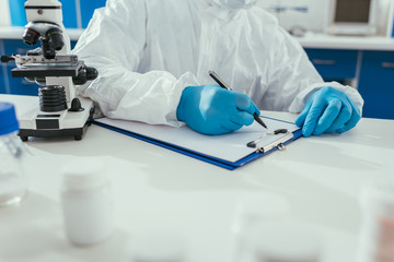 cropped view of biochemist writing results on clipboard in laboratory
