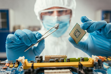 selective focus of engineer holding small stone with tweezers and microchip near computer...