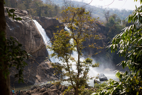 A huge waterfall Athirapally in Kerala, India. White streams of water of the waterfall break into small splashes and flow in a strong stream, Indian tourists look at the attraction