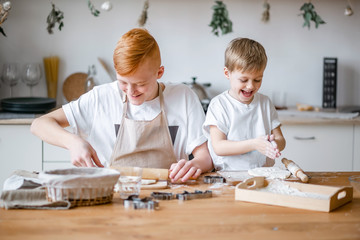 Two brothers cook in the kitchen.Family. A teenage boy with red hair and a small blond boy are making dough at a table in a light interior