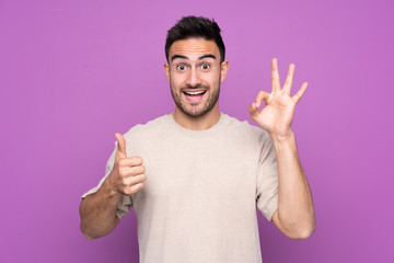 Young handsome man over isolated purple background showing ok sign and thumb up gesture