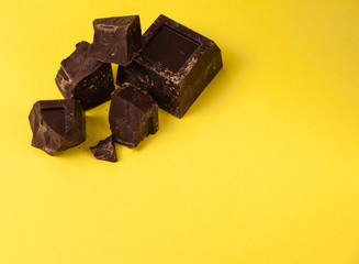 Appetizing pieces of black chocolate isolate on a yellow background close-up, copy space from right
