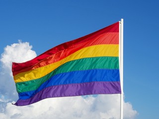 Rainbow Gay Pride Flag on blue sky  with white clouds background, Miami Beach, Florida, USA