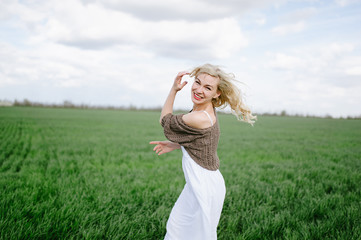  blonde girl in a white dress sits on the green fresh spring grass, blue sky