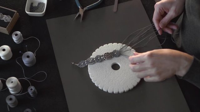 Lifestyle concept, reinvent your life and your job: close-up detail in low angle view of woman hands making macrame knotted bracelet with the fingers knotting the nylon thread on the kumihimo